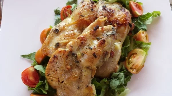 A plate of marinated chicken pieces on a bed of tomato and salad leaves: Pollo Dorato