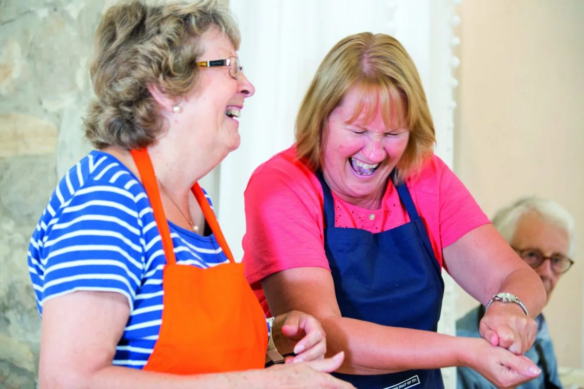 Two older women laughing together as they cook