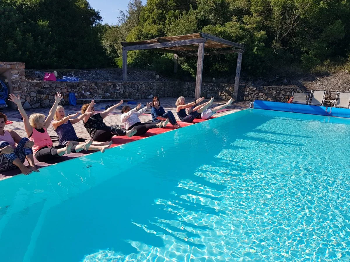 Group of older women practicing Pilates by the pool